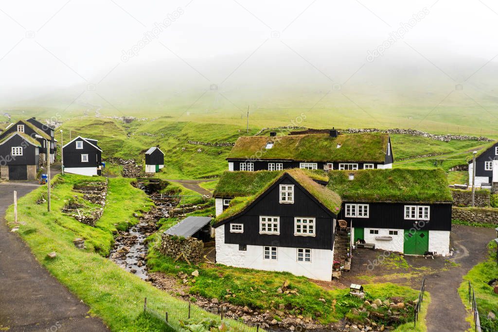 Mykines village rural landscape with grass-roof houses , small river and green hills.