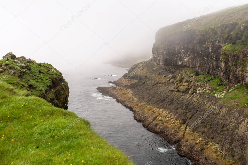 Cliff landscape on Mykines island in the morning with fog coming from the ocean.