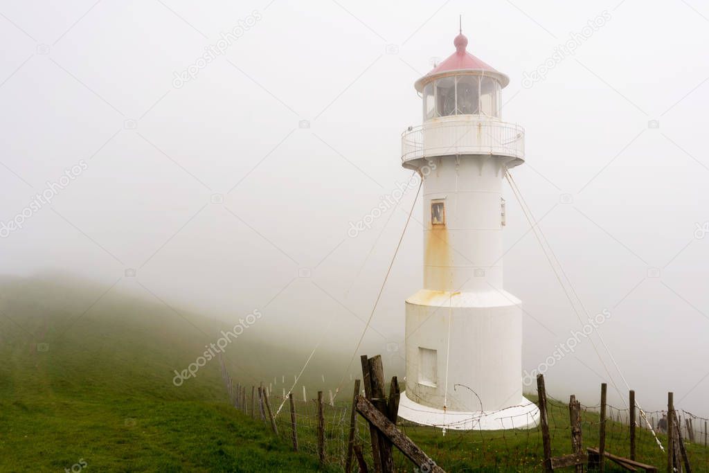 Foggy landscape and old lighthouse building. Mykines island, Faroe.