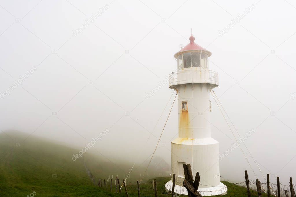 Old lighthouse building covered with thick fog on Mykines island, Faroe.