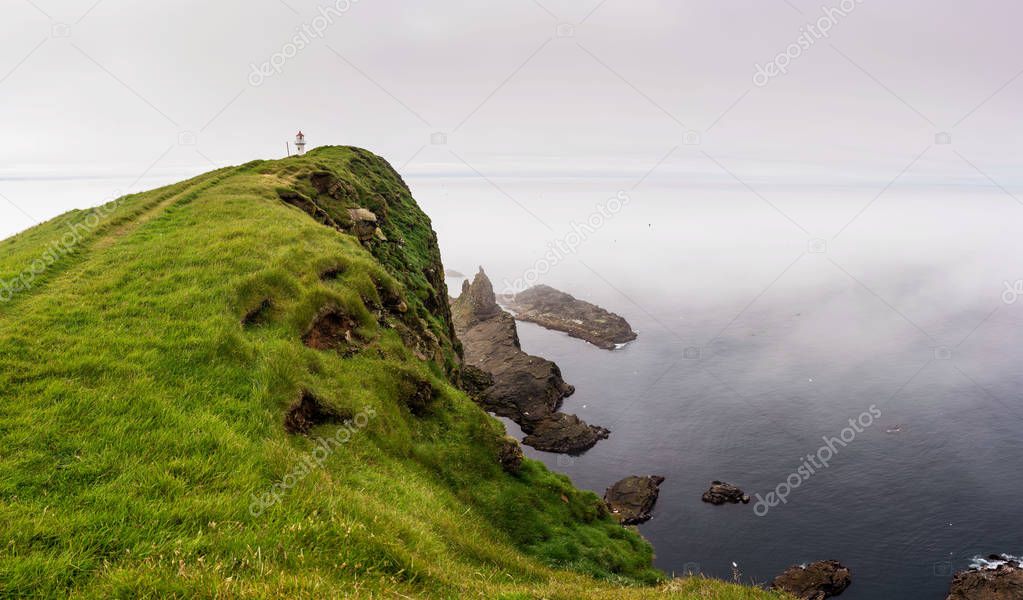 Panoramic landscape of Mykines island with lighthouse and cliffs above the ocean. Faroe Islands.