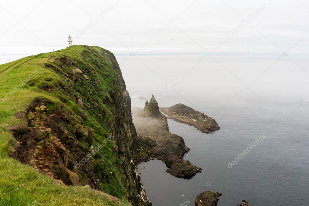 Foggy landscape of Mykines island with lighthouse at the end of island above ocean. Faroe Islands.