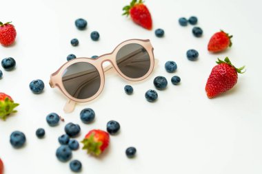 Çilek, yaban mersini ve pembe güneş gözlüğü düz arka plan yatıyordu.