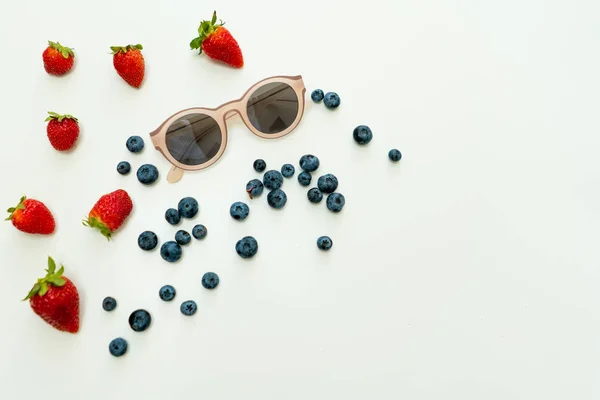 Summer flat lay with berries and sunglasses and copy space on right.
