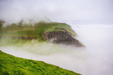 Mykines adasının yeşil dağları ve okyanustan gelen kene sisi. Faroe Adaları.