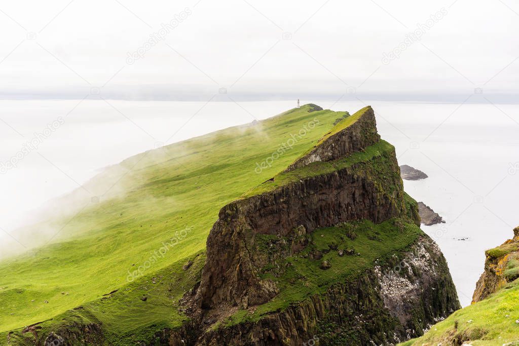 Mykinesholmur cliffs with nesting birds and a lighthouse on horizon. Mykines, Faroe Islands.