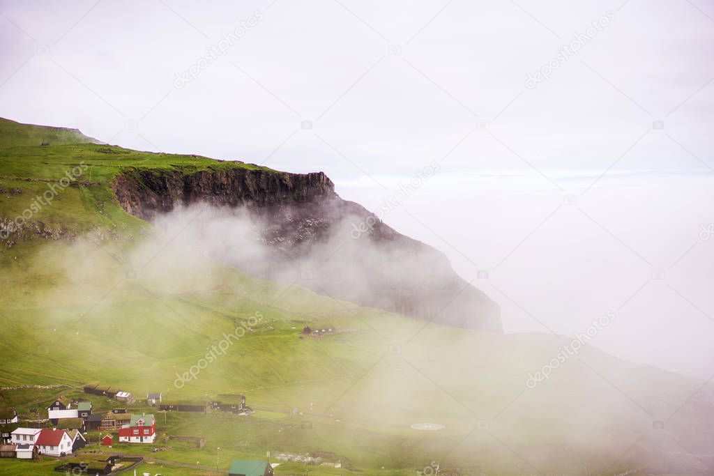 Misty landscape of Mykines island with small village and green mountain covered with fog. Faroe Islands.