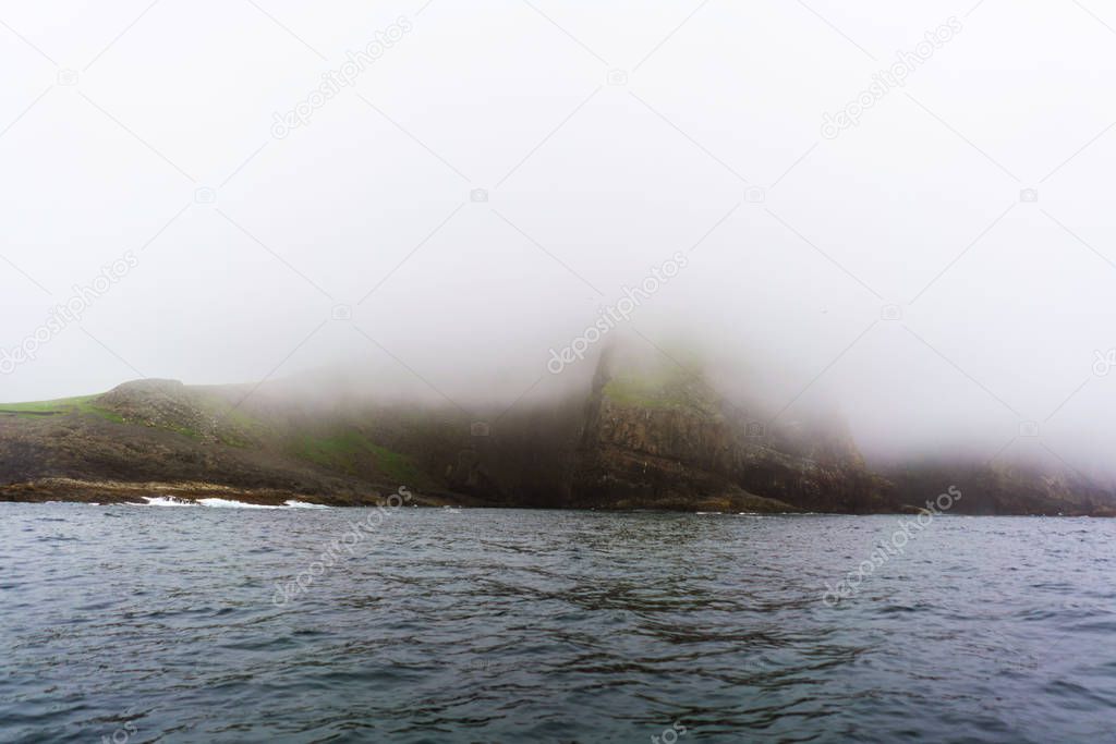 Foggy cliffs of Mykines island from water. Faroe Islands. 