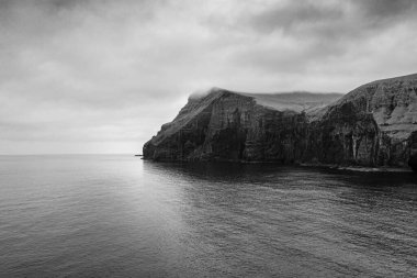 Okyanusun üzerindeki kayalıkların siyah beyaz manzarası. Faroe Adaları, Danimarka.