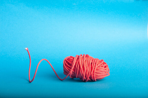 Twine of red color coiled into a ball on a blue background