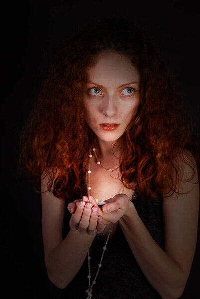 Beautiful red-haired woman holding a candle, on a dark background