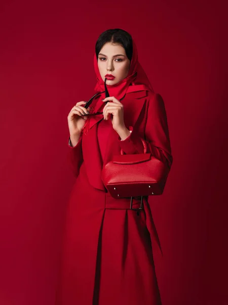 Waist up portrait of attractive model with bright make up looking at camera. She is wearing red coat and holding a handbag. fashion model.red lipstick. Hight fashion portrait