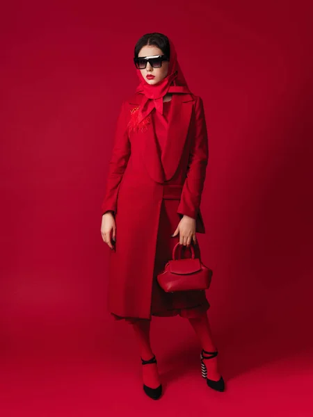 Waist up portrait of attractive model with bright make up looking at camera. She is wearing red coat and holding a handbag. fashion model.red lipstick. Hight fashion portrait