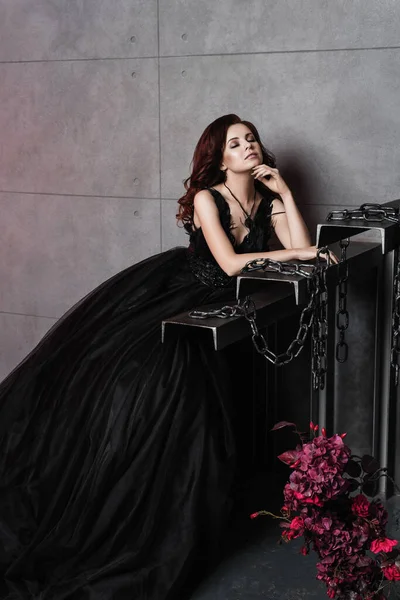 Genç, güzel, esmer bir kadın saray odasında dikiliyor. Cadılar Bayramı kızı. Siyahlı bir kızın portresi.