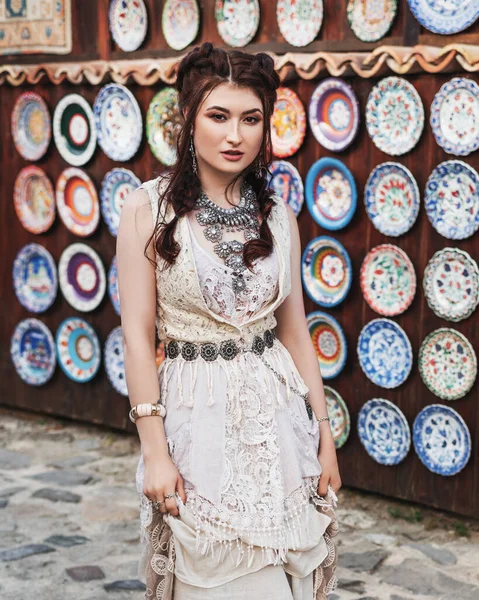Fashion girl wearing bohemian clothing posing in the old city street. Boho chic fashion style.Original dress end  jewerly.Stylized portrait of a beautiful girl , in light clothes, in etno-style