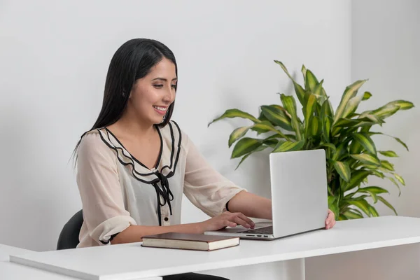 Latin bir kadın iş yerinde laptopuyla gülümsüyor. 
