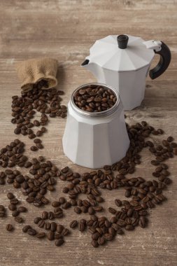 Kahve çekirdekli beyaz kahve demliği ve ahşap bir masanın üzerinde pipet örtüsü.