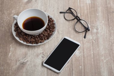 Porselen kahve çekirdekli ahşap ofis masası, okuma gözlüğü ve bir telefon.