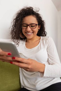 Ofisteki yeşil bir kanepede otururken gülümseyen Latin kadın.