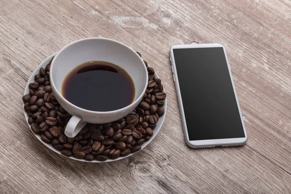 Kahve fincanı içinde kahve çekirdekleri ve ahşap bir masada ofis için bir telefon.
