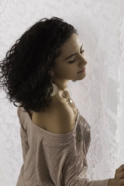 beautiful latin woman in a pink blouse showing shoulder, curly hair, natural light through a textured fabric, pink