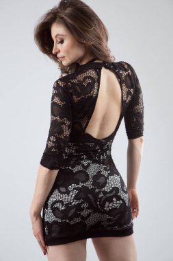 İnce beyaz tenli Latin bir kadın, siyah dantelli elbisesiyle sırt üstü duruyor, yüzü profilli, stüdyo.