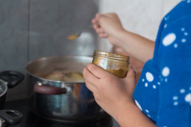 Mavi elbiseli bir insan ellerinde sarı baharat tutarken tencere kaynatıyor.