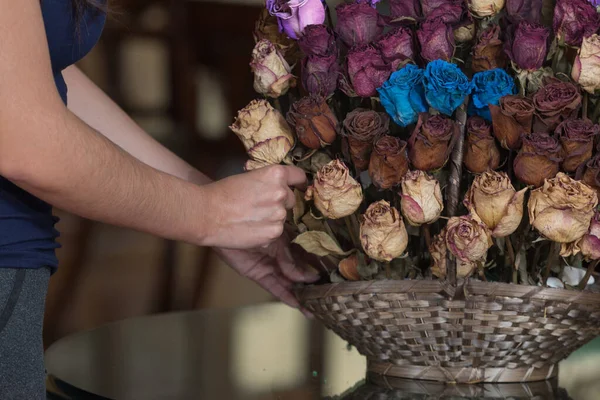 person placing a flower in arrangement with dried flowers of different colors, like potting a wicker basket, blurred background