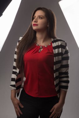 Beyaz tenli, uzun saçlı, kırmızı bluz ve siyah beyaz çizgili bir ceket giyen genç bir kadının fotoğraf çekimi. Profesyonel ışık ve gri arka planlı bir stüdyoda çekilmiş bir fotoğraf.