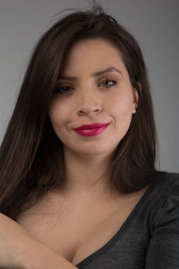 Uzun düz saçlı, açık renk gözlü ve makyajlı genç beyaz tenli kadın gülümsüyor, dosdoğru ileriye bakıyor, stüdyo çekimi.