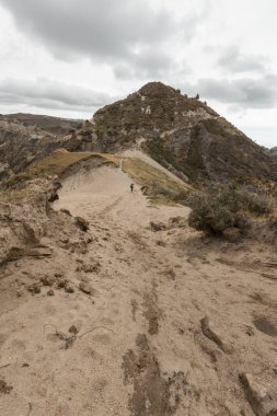 And Dağları 'nda kumlu bir yol manzarası, bulutlu gökyüzü ve yerel bitki örtüsü