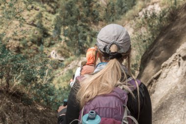 Sıcak güneşli bir günde, bir şapka ve seyahat valiziyle dağlarda yürüyüş yapan kadın bir gezgin.