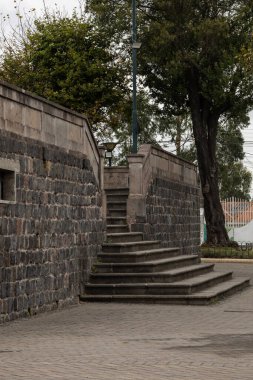 Çevresinde tarihi bir şehir parkında bulunan duvarları ve ağaçları olan taştan bir merdiven..