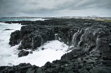 Dalgalar İzlanda 'nın siyah kayalıklarına çarpıyor.