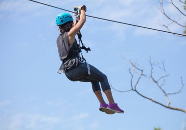Genç bir kadın parkta ipe tırmanıyor.