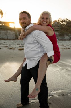 Kumsalda gün batımında gülümseyen çift sana bakıyor.