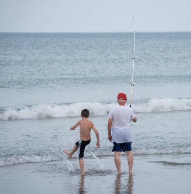 Baba ve oğul sahilde balık tutuyor.