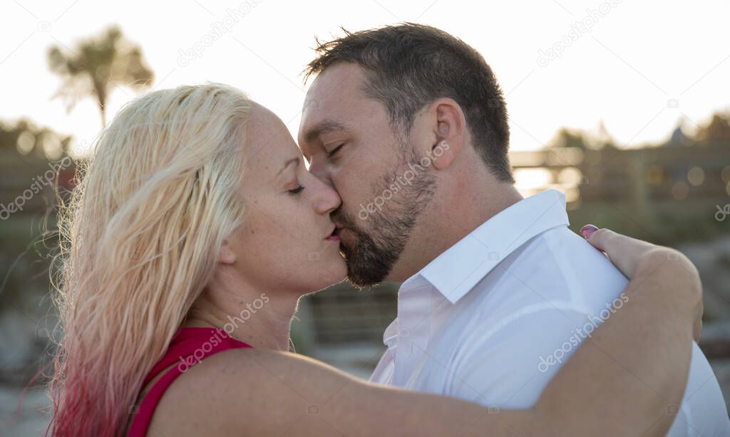 couple closes eyes to kiss passionately at sunset