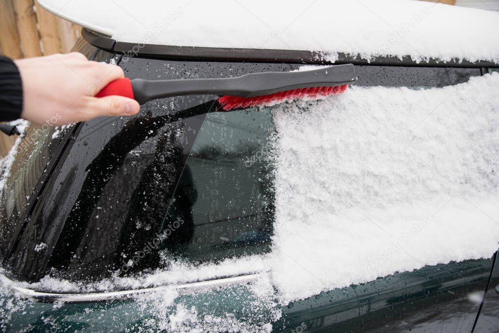 man brushes snow of car with snow brush