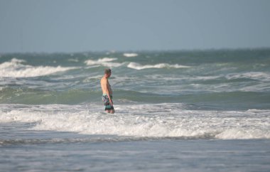 Kumsalda koşan dalgıç kıyafetli genç adam.