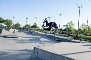 Patenciler ve motorcular numaralarını güneşli bir yaz gününde halka açık olan açık bir kaykay parkında yapıyorlar.