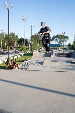 Patenciler ve motorcular numaralarını güneşli bir yaz gününde halka açık olan açık bir kaykay parkında yapıyorlar.