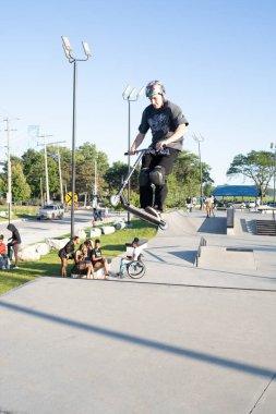 Patenciler ve motorcular numaralarını güneşli bir yaz gününde halka açık olan açık bir kaykay parkında yapıyorlar.