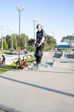 Patenciler ve motorcular numaralarını güneşli bir yaz gününde halka açık olan açık bir kaykay parkında yapıyorlar.