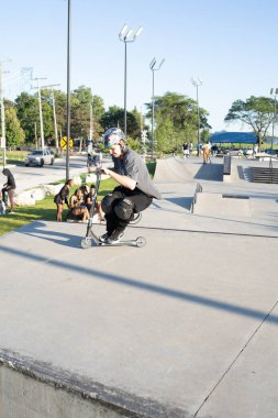 Patenciler ve motorcular numaralarını güneşli bir yaz gününde halka açık olan açık bir kaykay parkında yapıyorlar.