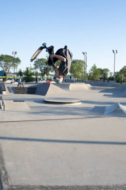 Patenciler ve motorcular numaralarını güneşli bir yaz gününde halka açık olan açık bir kaykay parkında yapıyorlar.