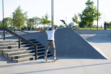 Patenciler ve motorcular numaralarını güneşli bir yaz gününde halka açık olan açık bir kaykay parkında yapıyorlar.