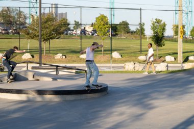 Patenciler ve motorcular numaralarını güneşli bir yaz gününde halka açık olan açık bir kaykay parkında yapıyorlar.