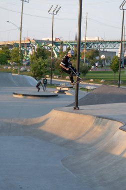 Kaykaycılar ve scooterlar numaralarını güneşli bir yaz gününde halka açık olan açık bir kaykay parkında yapıyorlar.