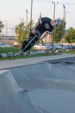 Kaykaycılar ve scooterlar numaralarını güneşli bir yaz gününde halka açık olan açık bir kaykay parkında yapıyorlar.